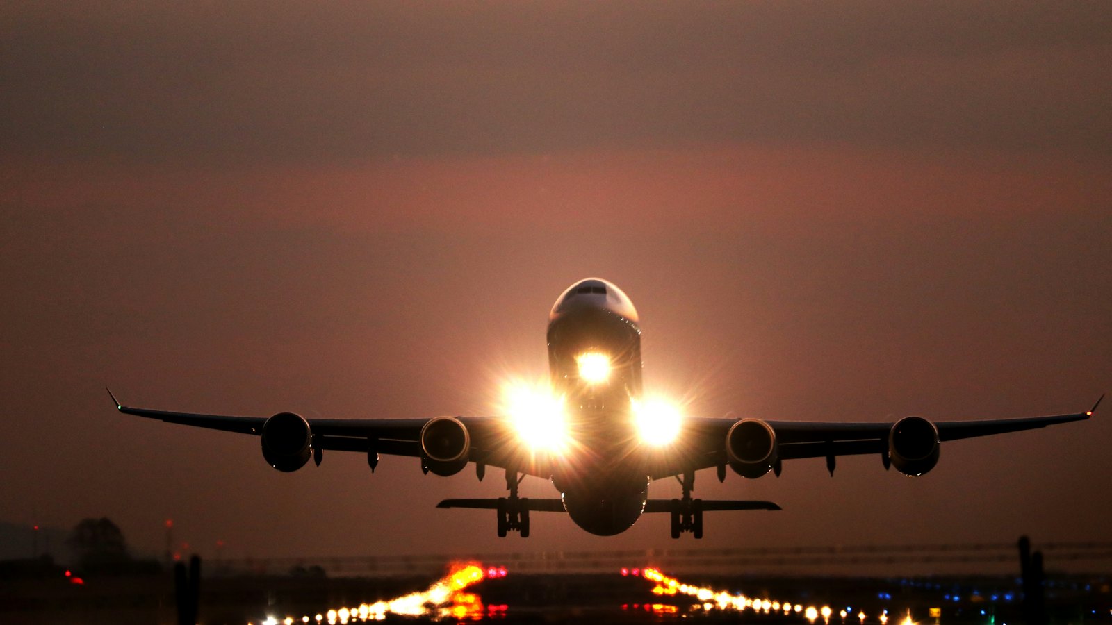 Passenger jet taking off at night above lit runway lights
