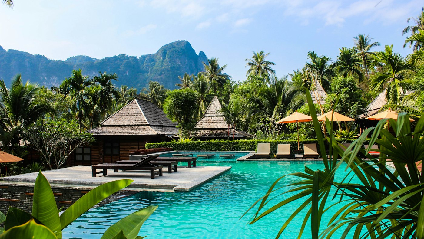 Resort pool surrounded by palms and thatched villas
